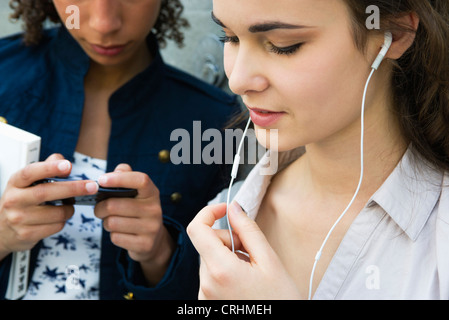 Jeune femme debout avec ami, listening to earphones