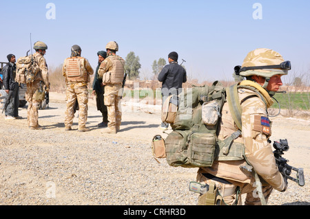 Soldats britanniques parler à un local suspectes alors qu'un jeune soldat fournit la couverture. Banque D'Images