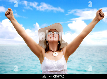 Jeune femme portant un chapeau blanc debout à la mer, avec les bras tendus Banque D'Images