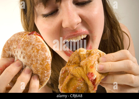 Une jeune femme de manger deux contre-beignes. Jam donuts ont été critiqués par la malbouffe des militants de la guerre globale sur l'obésité comme insalubres avec faible valeur nutritionnelle. Le terme 'junk food' a été créée par Michael Jacobson, Directeur du Centre pour la science dans l'intérêt public, pour décrire des aliments qui contiennent des niveaux élevés de contenu de graisses saturées, de sel, ou suga Banque D'Images