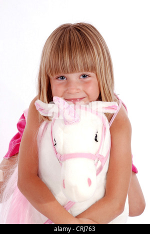 Petite fille blonde équitation une licorne en peluche Banque D'Images