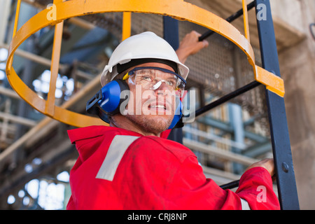 Worker climbing ladder à la raffinerie de pétrole Banque D'Images