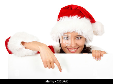 Smiling young woman in a Santa's dress pointant sur le panneau blanc vide en face d'elle Banque D'Images