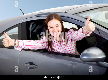 Jeune femme se pencher hors de la fenêtre d'une voiture avec un sourire et les deux pouces vers le haut Banque D'Images