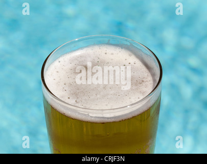 Un verre de pinte de bière lager froid assis sur le bord de piscine bleu Banque D'Images