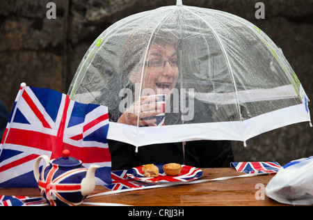 Les refuges d'une femme de la pluie au cours d'une partie de la rue de la célébrations du Jubilé de diamant de la Reine à Morecambe, UK. Banque D'Images