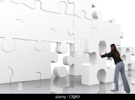 Jeune femme essayant de monter une pièce en un gigantesque puzzle tridimensionnel mur blanc Banque D'Images