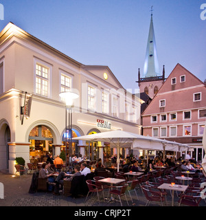 Les gens siiting dans un restaurant de la rue sur la place du marché de Unna à heure bleue, l'église de la tour illuminée, Stadtkirche, dans l'arrière-plan, l'Allemagne, en Rhénanie du Nord-Westphalie, Ruhr, Unna Banque D'Images