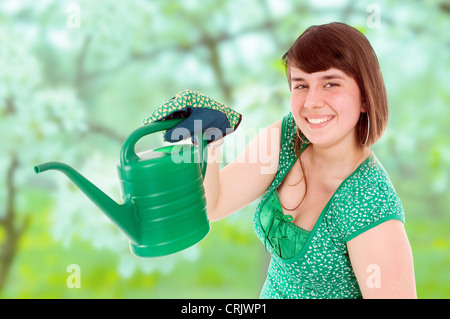 Smiling brunette jeune fille avec un chemisier vert dcollet avec dessin de fleurs et d'un arrosoir dans le jardin Banque D'Images