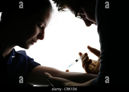 La silhouette d'un médecin l'élaboration d'un échantillon de sang au bras d'une jeune patiente. Banque D'Images