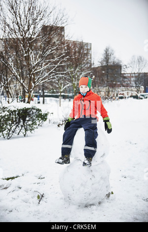 Garçon assis sur snowman in park Banque D'Images