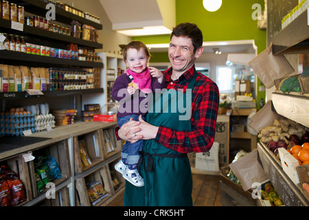 Grocer holding daughter in store Banque D'Images