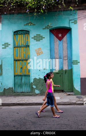 Deux filles marcher dans les rues de la vieille Havane Cuba, avec un drapeau cubain et viva Cuba libre peint sur deux portes en arrière-plan. Banque D'Images