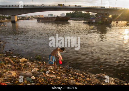 La vie sur la rivière à Saigon. Un homme à la recherche de ce qui est récupérable à partir de la poubelle Banque D'Images