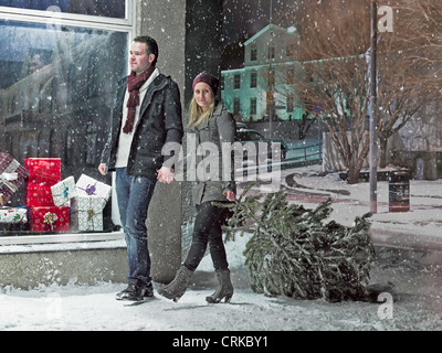 Couple carrying Christmas Tree in snow