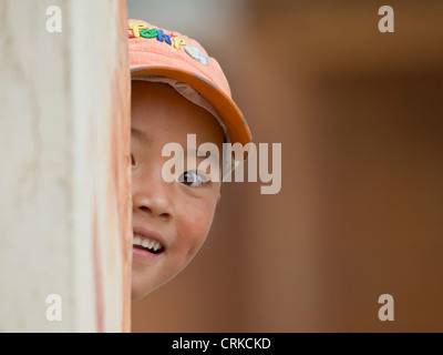 Un jeune garçon chinois tibétain jouant à cache-cache autour d'un coin à l'appareil photo. Banque D'Images
