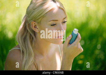 Une jeune femme blonde assise dans l'herbe à l'aide d'un inhalateur d'asthme Banque D'Images