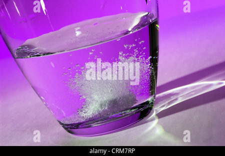 Un comprimé effervescent se dissout dans un verre d'eau contre un fond violet. Banque D'Images