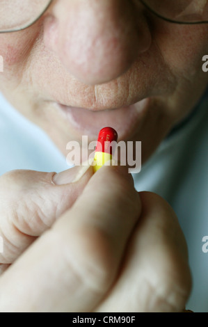 Homme âgé de placer la pilule rouge et jaune dans sa bouche. Banque D'Images