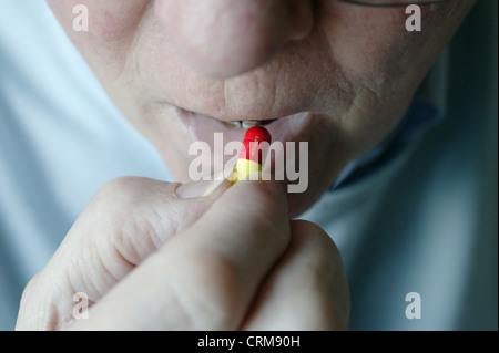 Homme âgé de placer la pilule rouge et jaune dans sa bouche. Banque D'Images