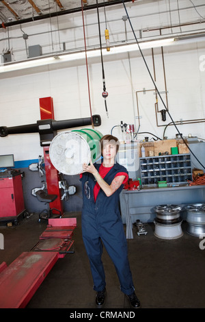 Portrait d'une jeune femme transportant du pétrole mécanicien tambour sur l'épaule dans un garage de réparation automobile Banque D'Images