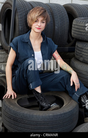 Portrait d'un jeune mécanicien assis sur des pneus de voiture en atelier Banque D'Images