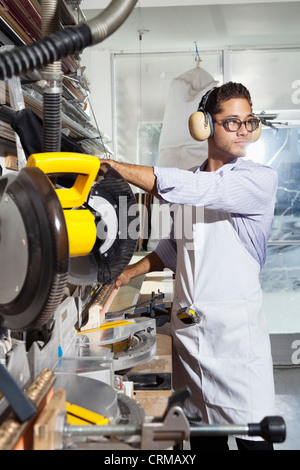 Jeune artisan avec des protections lors de l'utilisation d'une scie circulaire Banque D'Images