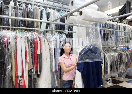 Portrait of a happy Mid adult woman putting plastique pour vêtements nettoyés à sec dans une laverie Banque D'Images