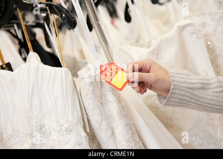 Cropped shot of female hands holding : étiquette attachée à robe de mariée en boutique Banque D'Images