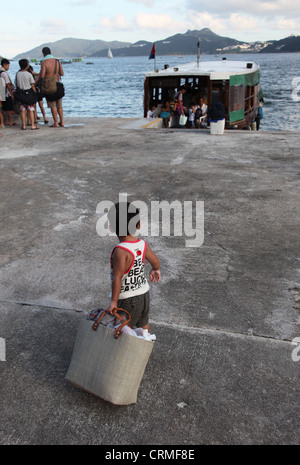 Un petit garçon tirant un gros sac sur un plancher vers un ferry ou bois junk pour aller à l'autre côté de la baie. C'est Hong Kong Banque D'Images