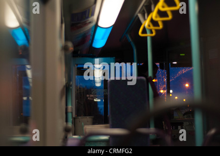 À l'intérieur d'un bus vide la nuit, montrant quelques réflexions de fenêtre ainsi que quelques lampadaires à l'extérieur Banque D'Images