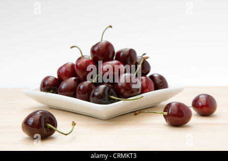 Les cerises mûres dans un bol et sur planche en bois à l'arrière-plan blanc Banque D'Images