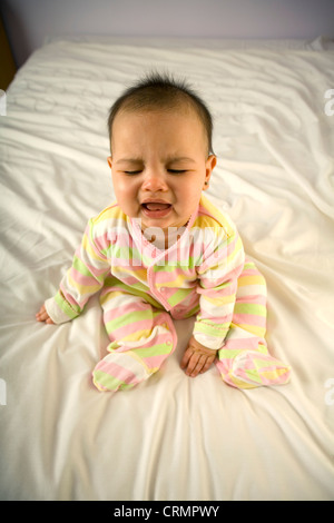 Une petite fille assise sur un lit en train de pleurer. Banque D'Images