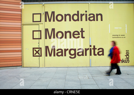 Une femme en passant devant un grand panneau publicitaire près du bâtiment Blue Fin sur Sumner Street dans le quartier londonien de Southwark. Banque D'Images