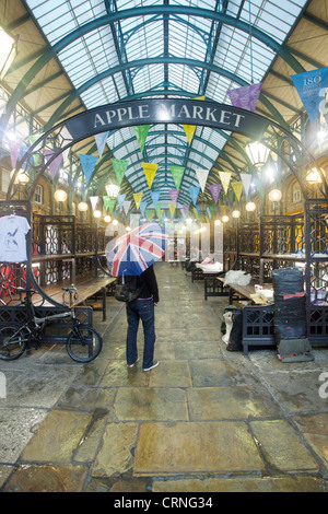 Un homme avec un parapluie Union Jack debout dans le marché d'Apple à Covent Garden. Banque D'Images