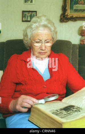 Une vieille femme avec une loupe pour lire une Bible. Banque D'Images
