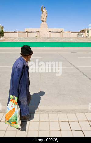 Un vieil homme chinois pauvres passe devant la statue de Mao Zedong à Kashgar. Banque D'Images