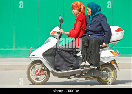 Une mère et sa fille Uygher Chinois voyagent le long d'une route sur leur scooter dans Kashgar. Banque D'Images