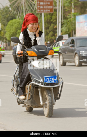 Une femme ouïghoure chinoise voyage le long d'une route sur son triporteur tout en parlant sur son téléphone portable à Kashgar. Banque D'Images