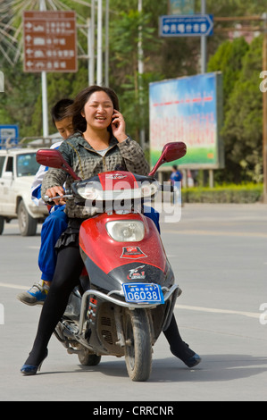 Une femme chinoise voyage le long d'une route sur son triporteur tout en parlant sur son téléphone portable à Kashgar. Banque D'Images
