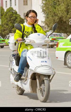 Une femme chinoise voyage le long d'une route sur son triporteur tout en parlant sur son téléphone portable à Kashgar. Banque D'Images