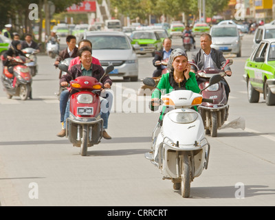 Une femme chinoise voyage le long d'une route sur son triporteur tout en parlant sur son téléphone portable à Kashgar. Banque D'Images