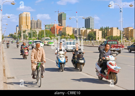 Un avis de personnes sur les scooters et bicyles voyageant le long d'une route principale dans la région de Kashgar. Banque D'Images