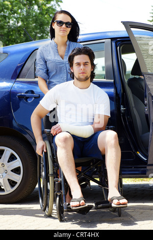 Jeune couple de quitter ou d'arriver à l'hôpital,jeune homme en fauteuil roulant avec un plâtre sur sa main. Banque D'Images