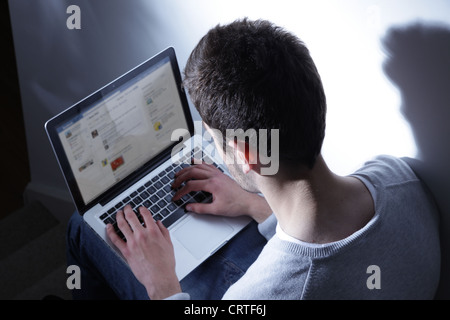 Jeune homme assis dans le noir avec son ordinateur portable, Ttweeting. Banque D'Images