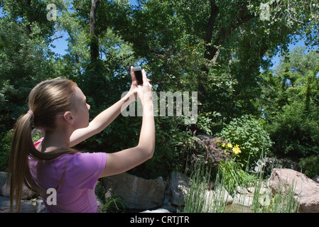 Une jeune fille de 13 ans prend une photo à l'extérieur à l'aide de son appareil photo de l'iphone. Banque D'Images