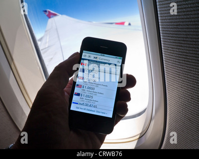 Taux de change historiques en vol sur smartphone avec fenêtre de cabine et ciel bleu derrière Banque D'Images