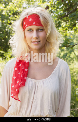 Belle jeune blonde adolescente avec bandana regardant la caméra. Portrait en été contre un fond vert floue Banque D'Images