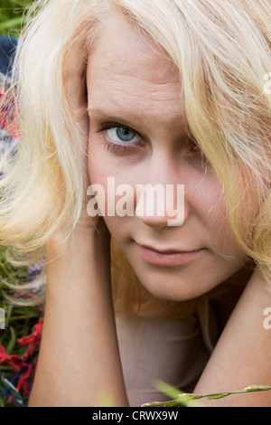 Cute young blonde woman lying on meadow looking pensive à l'appareil photo. Portrait en été comme close up Banque D'Images