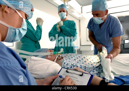 Une équipe de chirurgiens se préparent à lancer une opération avec le patient anesthésié déjà à proximité. Banque D'Images